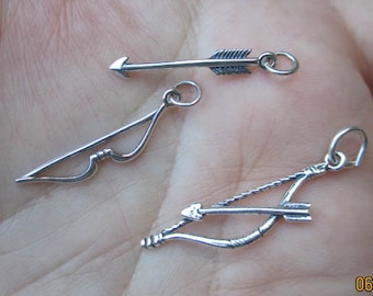 May include: Three silver-toned charms: an arrow, a bow, and a bow with an arrow. The arrow charm is a simple, straight design. The bow charm has a curved shape. The bow and arrow charm has a string and arrow.