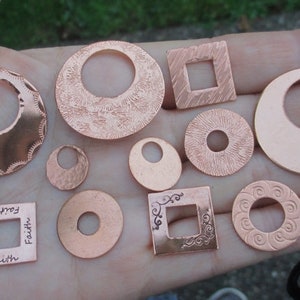 Puede incluir: Una colección de diez dijes de metal de cobre con varias formas y diseños, incluyendo círculos, cuadrados y un dije con la palabra "Faith" inscrita en él.