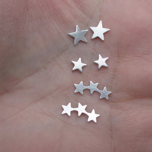 May include: A set of silver star-shaped earrings. The earrings are arranged in a line, with the largest star in the centre and the smaller stars on either side.