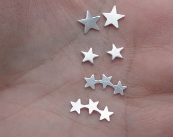 May include: A set of silver star-shaped earrings. The earrings are arranged in a line, with the largest star in the center and the smaller stars on either side.