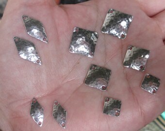 May include: A collection of silver-toned metal charms with a hammered texture. The charms are in the shape of squares and diamonds, with two holes in each charm.