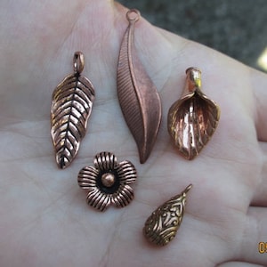 May include: Five copper-coloured metal charms, including a flower, a teardrop, and three leaf shapes.