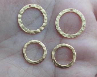 May include: Four gold-colored hammered metal circle charms. Two larger circles have a small hole at the top, and two smaller circles are below. These charms are ideal for jewelry making and crafting.