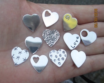 May include: A collection of 10 silver heart-shaped charms with various designs, including a heart with a hole, a heart with a swirl design, a heart with the word "Love" engraved, and a heart with a star pattern.