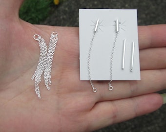 May include: Two pairs of silver earrings. One pair features a long, dangling chain with a small, silver bar at the top. The other pair features a short, straight silver bar.