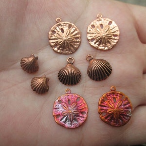 May include: Assortment of copper-toned metal charms in the shape of seashells and sand dollars. The charms have a rustic, antique finish.
