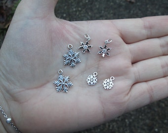 May include: Five silver snowflake charms of varying sizes. The charms are delicate and intricate, with a variety of snowflake designs.
