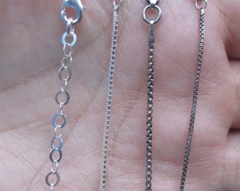 May include: Close-up of four different silver chain necklaces. The chains vary in style, including a delicate circle chain, a box chain, and a curb chain. Each chain has a clasp for secure wear.