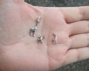 May include: Three silver giraffe charms, two are standing and one is laying down. The charms are on a person's hand.