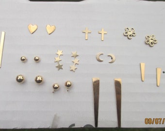 May include: Assortment of gold-toned metal earring charms, including hearts, crosses, stars, moons, and geometric shapes.  The charms are arranged on a white surface. 09/07/2018 is written in the bottom right corner of the image.