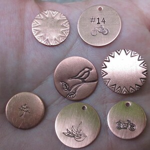 May include: Seven round copper-coloured metal tags with various designs. One tag features a bicycle design and the text '#14'. Another tag has a bird on a branch design. Another tag has a tree design. Another tag has a bird in flight design. Another tag has a motorcycle design. Two tags have a starburst design.