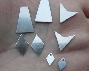 May include: A collection of eight silver metal shapes, including triangles, diamonds, and rectangles. The shapes are arranged on a hand.