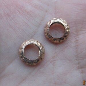 May include: Two gold-toned metal rings with a textured surface. The rings are round and have a hole in the center.