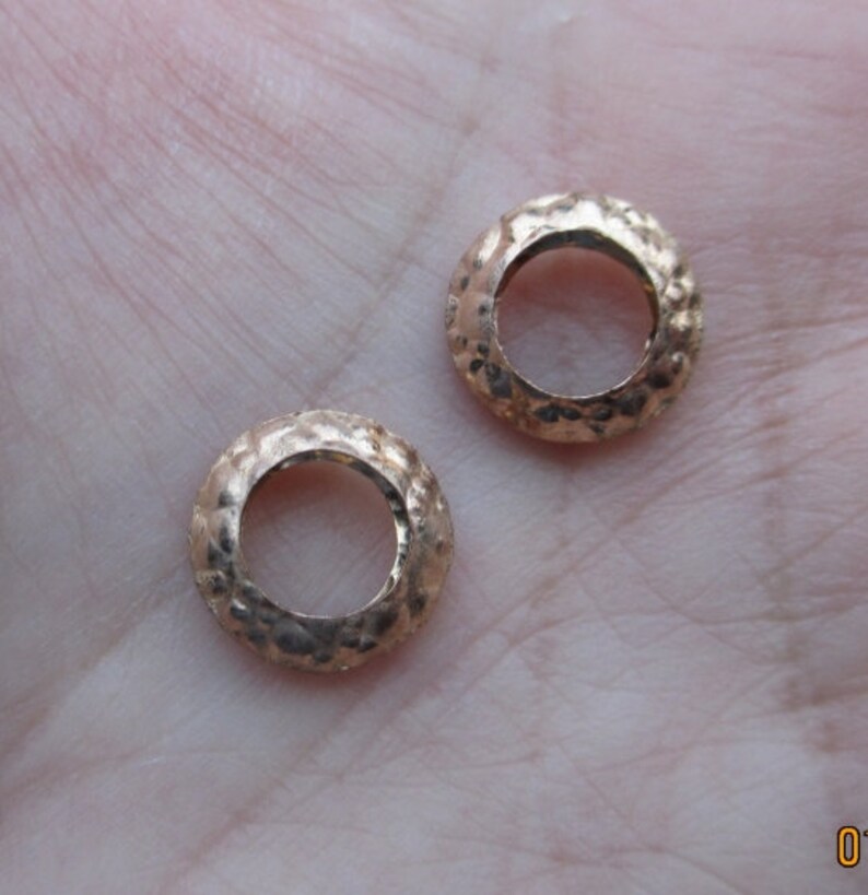 May include: Two gold-toned metal rings with a textured surface. The rings are round and have a hole in the center.