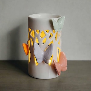Könnte beinhalten: Weißer Keramik-Öldiffusor mit Baumdesign und vier Schmetterlingsakzenten in den Farben Rosa, Lila, Orange und Grün.