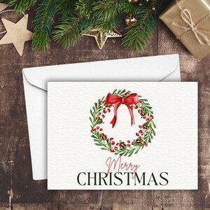 以下が含まれることがあります： 赤いリボンと赤い実のついた緑のリースが描かれた白いカード。黒い文字で「Merry Christmas」と書かれている。