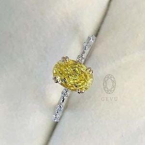 May include: A silver ring with a yellow oval-cut gemstone. The band is adorned with small, clear stones. The ring is presented in a blue jewellery box, highlighting the vibrant yellow of the central stone.