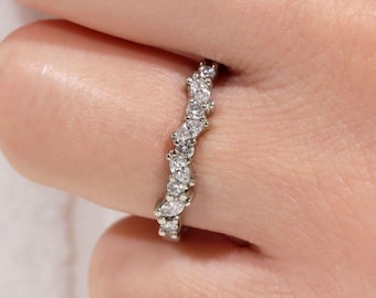 May include: A silver ring with a wavy design, set with multiple clear, sparkling gemstones. The ring is worn on a finger, showcasing its delicate and elegant appearance. The gemstones are of varying shapes, adding visual interest.