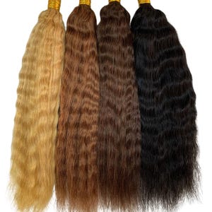 May include: Four bundles of wavy hair extensions in varying shades of blonde, brown, and black. Each bundle is secured at the top with a gold-colored band. The hair has a natural, textured appearance, suitable for adding length and volume.