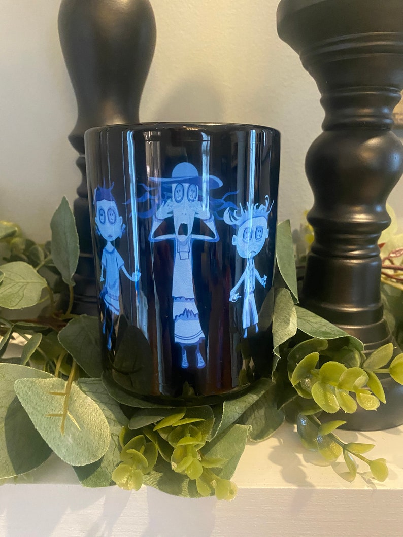 May include: Black ceramic mug with a blue and white cartoon image of three characters with large eyes. The characters are wearing hats and are looking surprised.