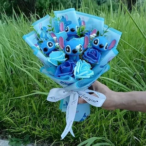 May include: A bouquet featuring blue artificial roses and several blue Stitch character figures. The arrangement is wrapped in light blue paper decorated with Stitch illustrations and tied with a white ribbon printed with the text For you.