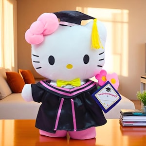 Könnte beinhalten: Ein Hello Kitty-Plüschtier in einem Abschlusskleid. Die Puppe ist weiß mit einer rosa Schleife, schwarzen Augen und einer gelben Nase und Fliege. Sie trägt eine schwarze Kappe und einen Umhang mit rosa Besatz und hält ein Diplom und Blumen.