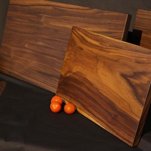 May include: Three walnut wood chopping boards of varying sizes and shapes. The largest board is rectangular, the medium board is rectangular with rounded corners, and the smallest board is freeform. All boards are made of dark brown wood with a natural grain pattern.