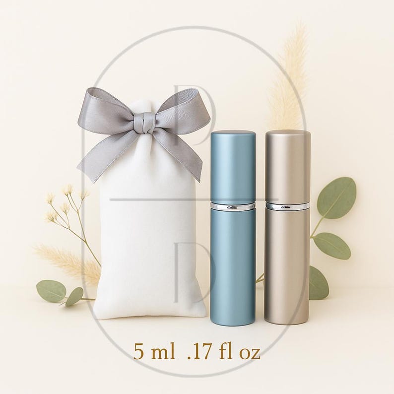 May include: Two perfume atomizers, one blue and one gold, next to a white pouch with a gray satin bow. The atomizers are labeled 5 ml / .17 fl oz. The background is a soft beige with decorative sprigs.