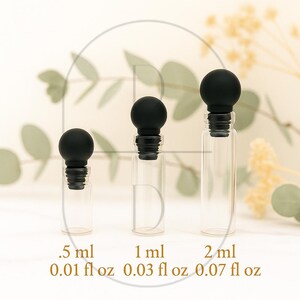 May include: Three clear glass bottles with black stoppers. The bottles are labeled with measurements: .5 ml, 1 ml, and 2 ml, and also with fluid ounces: 0.01 fl oz, 0.03 fl oz, and 0.07 fl oz. The bottles are arranged in a row.