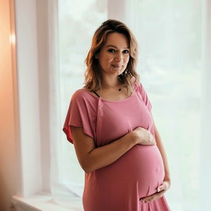 Plus Size pregnant mom wearing a light pink hospital delivery gown to deliver her baby. Fabric is soft and stretchy with snaps at shoulder for breastfeeding and down back for epidural. Long enough to cover knees. Favorite baby shower gift from Mom.