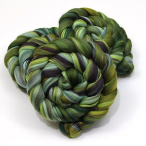 May include: Two skeins of hand-dyed yarn in shades of green, teal, and purple. The yarn is tightly twisted, creating a braided appearance. The colors blend together, creating a variegated effect. The yarn is likely made of wool or a similar fiber.