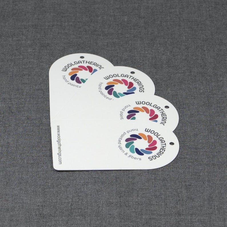 May include: Four white, rounded-top rectangular tags stacked in a fan shape. Each tag features a circular logo with colorful segments and the text Woolgathering, hand painted, and yarn & fibers. The website www.woolgatherings.com is printed on the side.
