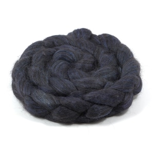 May include: A thick, coiled bundle of dark navy blue wool roving, arranged in a circular, braided pattern. The fiber has a soft, fuzzy texture with visible strands of deep blue and black tones intertwined throughout the dense, circular mass.