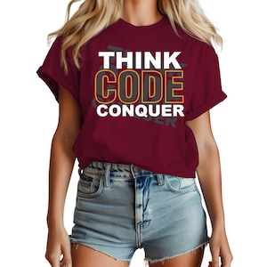 Op de afbeelding: Een bordeauxrood t-shirt met de woorden "THINK CODE CONQUER" in witte en oranje letters. Het shirt wordt gedragen met een spijkerbroekshort. Het algemene thema is gerelateerd aan technologie en coderen.
