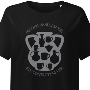 May include: Black t-shirt with a gray graphic of pottery and mugs. The text reads "PULLING HANDLES? YES. EYE CONTACT? NEVER."