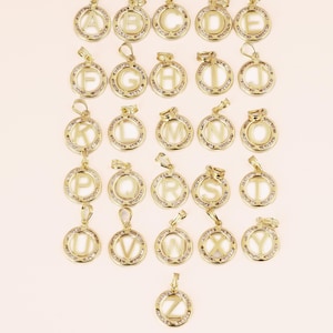 May include: A collection of gold-colored alphabet pendants, each featuring a letter from A to Z. The pendants are round, with a clear center and a border of small, sparkling stones. Each pendant has a loop for a chain.