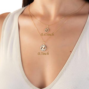 May include: Two gold necklaces with pendant charms. The top necklace has a small, round pendant with the letter "K" and is 0.45 inches in diameter. The bottom necklace has a larger, round pendant with the letter "Z" and is 0.7 inches in diameter.