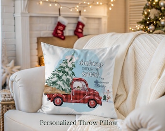 May include: White throw pillow with a Christmas theme. The pillow features a red truck carrying a Christmas tree, with the text "Dashing Through The Snow." The Henderson Family is also printed on the pillow. Snowflakes and a light blue background complete the design.