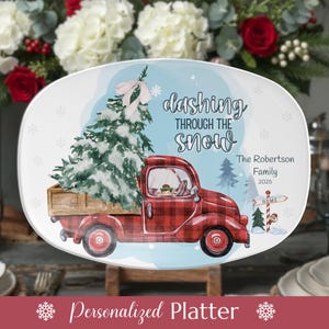 May include: Oval white platter with a Christmas theme. A red plaid truck carries a snow-covered Christmas tree. Text reads "Dashing Through The Snow" and "Personalized Platter". Includes family name and year.