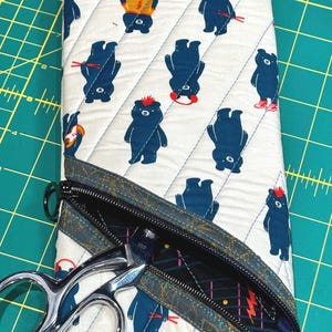 May include: A white zippered pouch with a blue and white patterned fabric featuring a repeating design of bears. The pouch is open and a pair of silver scissors are inside.