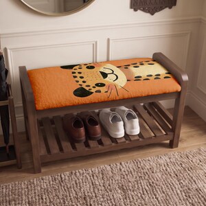 May include: A wooden shoe bench with a cushioned seat featuring an orange leopard print graphic. The bench has a slatted lower shelf holding a pair of brown leather shoes and a pair of white sneakers. An umbrella stand with two black umbrellas sits nearby.