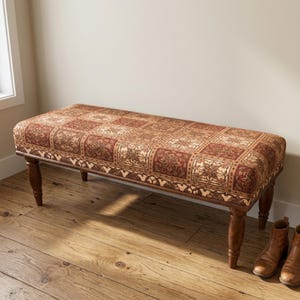 May include: A rectangular upholstered bench featuring a patchwork-style fabric seat with repeating floral and geometric patterns in shades of rust, brown, and cream. The bench is supported by four turned wooden legs with a dark brown finish.
