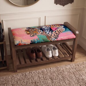 May include: A wooden entryway bench with a cushioned seat featuring a colorful leopard print design. The bench has a slatted lower shelf holding a pair of brown leather shoes and a pair of white sneakers. An umbrella stand with two umbrellas sits nearby.