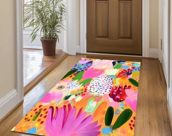 Op de afbeelding: Een kleurrijk vloerkleed met een bloemenpatroon. Het vloerkleed heeft roze, oranje, gele, groene en blauwe bloemen op een witte achtergrond.