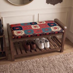 Può includere: Una panca scarpiera in legno con un cuscino rettangolare caratterizzato da un motivo floreale multicolore nei toni del rosso, blu e crema. La panca presenta un ripiano inferiore a doghe con un paio di scarpe marroni e un paio di sneakers bianche.
