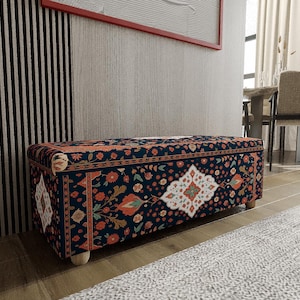 Könnte beinhalten: Ein rechteckiger Hocker mit einem dunkelblauen Blumenmuster und Holzbeinen. Das Design umfasst orange, weiße und grüne Blumenmotive. Der Hocker steht in einem Raum mit einer gestreiften Wand und einem neutralfarbenen Teppich.