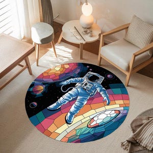 Könnte beinhalten: Ein runder Teppich mit einem bunten Glasmosaik-Design, das einen Astronauten zeigt, der im Weltraum schwebt. Der Teppich hat einen dunkelblauen Hintergrund mit bunten Planeten und Sternen.