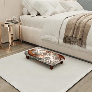 May include: A rectangular footstool with a tiger design. The top features a detailed illustration of a tiger with orange and black stripes, surrounded by floral and geometric patterns. The stool has four dark brown legs and is placed on a white rug.