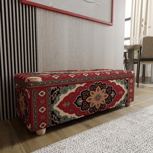 May include: A rectangular storage bench featuring a vibrant red, cream, and teal floral pattern reminiscent of a traditional rug. The bench is supported by four small, light-colored wooden feet and has a flat, upholstered top surface.