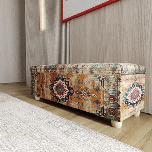May include: A rectangular ottoman with a patterned fabric in shades of orange, blue, and red. The design features geometric and floral motifs. The ottoman sits on four short, rounded, light-colored wooden legs. The overall style is reminiscent of a vintage rug.